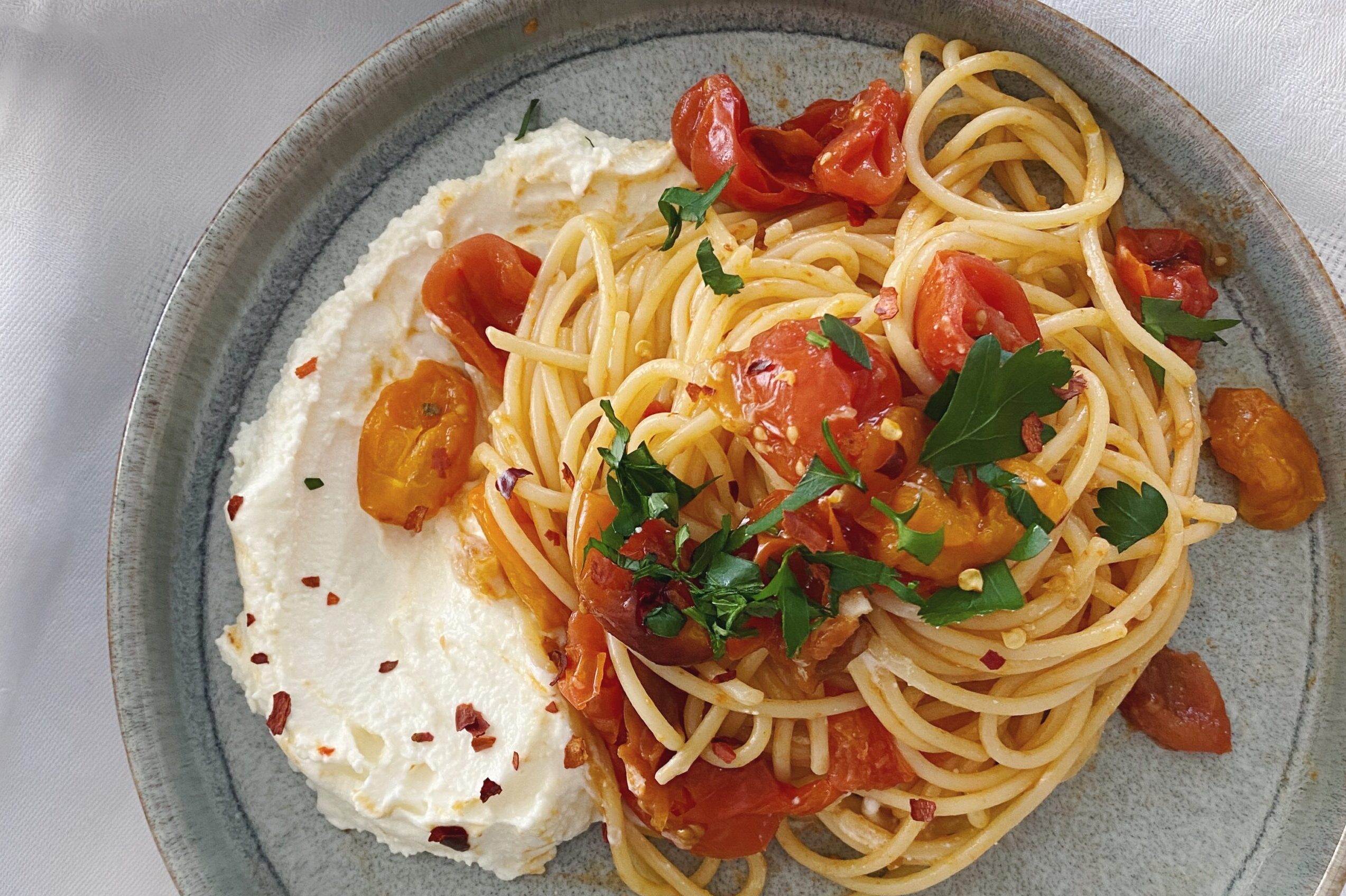 Spaghetti mit gebackenen Tomaten und einer Feta-Crème auf einem blau-grauen Teller angerichtet