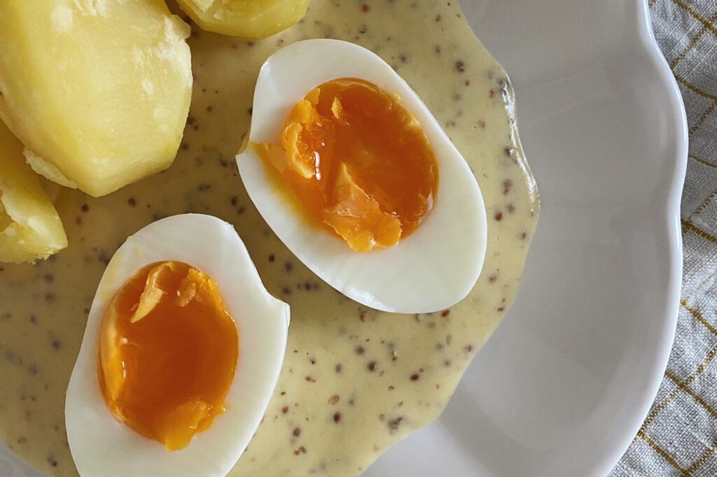 Zwei halbierte Eier auf Senfsauce mit Kartoffeln in einem weissen Teller angerichtet
