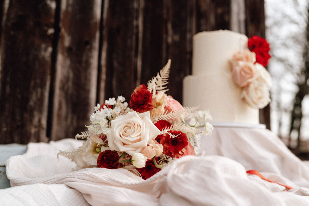 Im Fokus des Bildes liegt der Brautstrauss vom Blumenladen Florium, passend zur Torte von Schneeweisschen und Rosenrot, welche im Hintergrund verschwommen vor einer dunklen Holzwand zu sehen ist (Bild von Cate Brodersen)